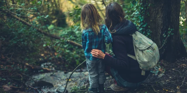 A young mother and her toddler are resting by a brook in the woods